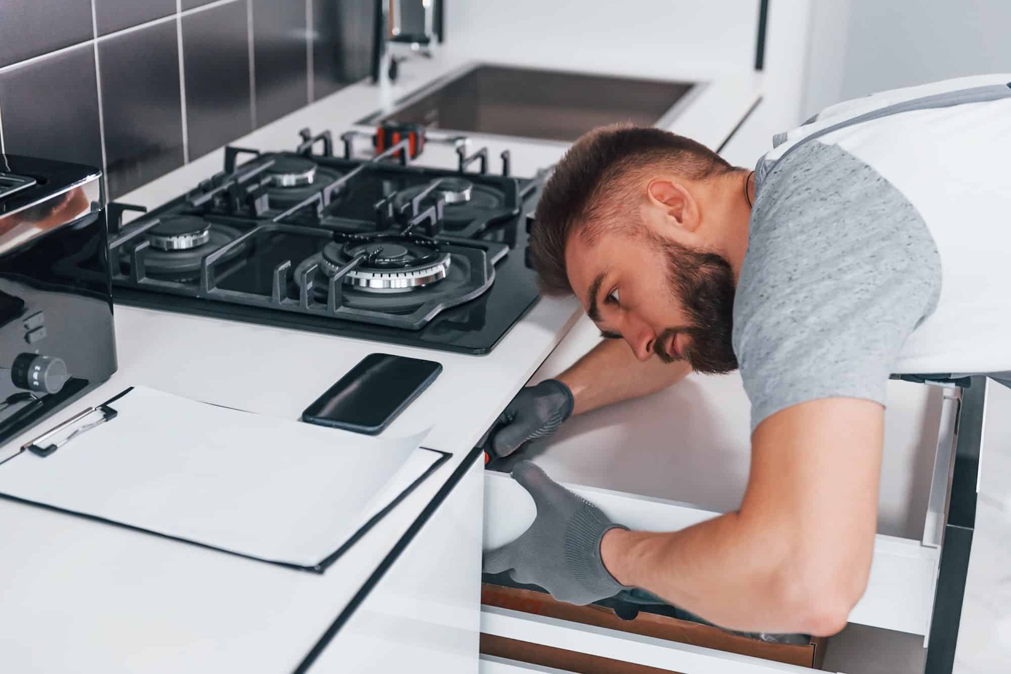 young professional plumber in grey uniform working on the kitchen 2